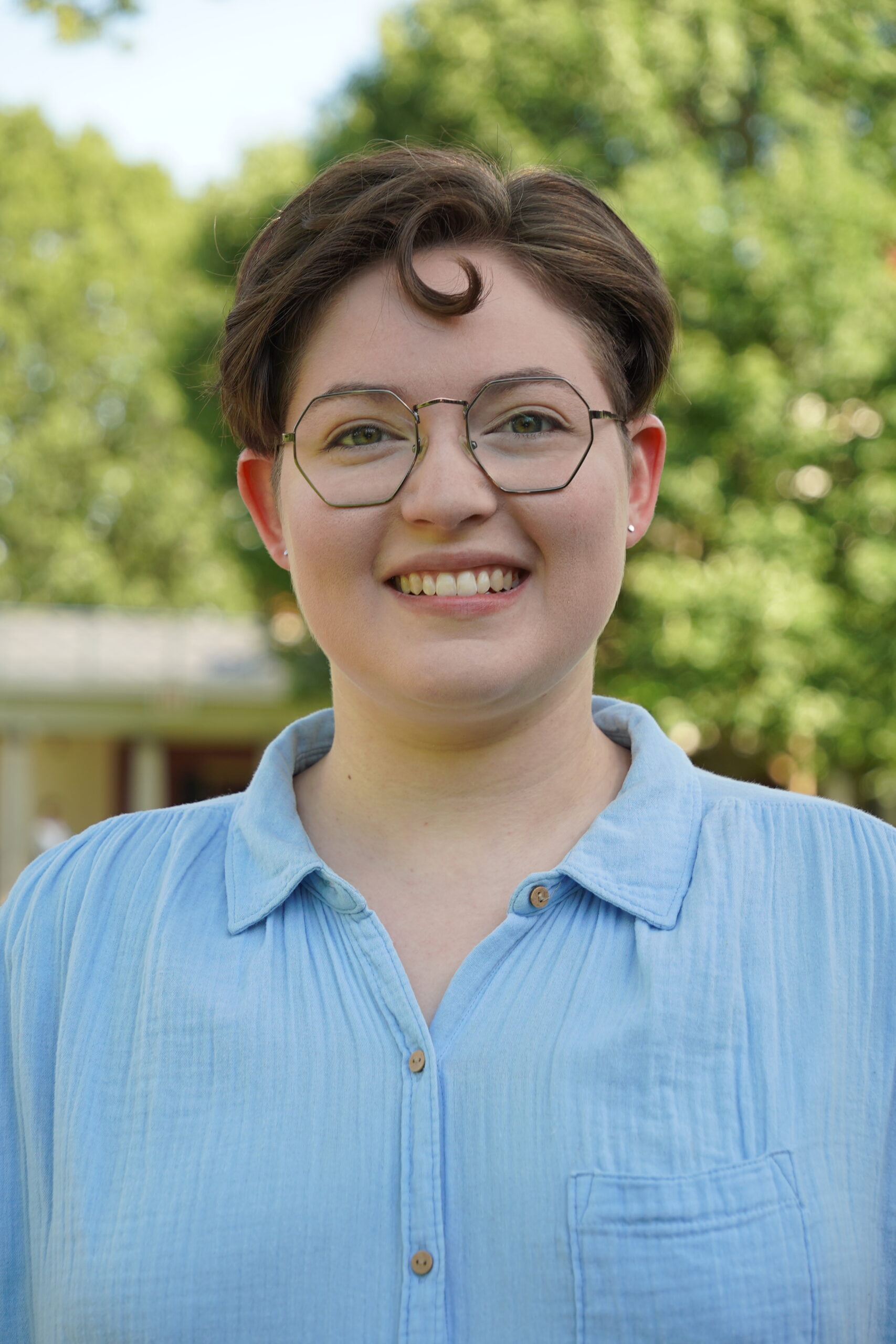White person standing and smiling in front of tree