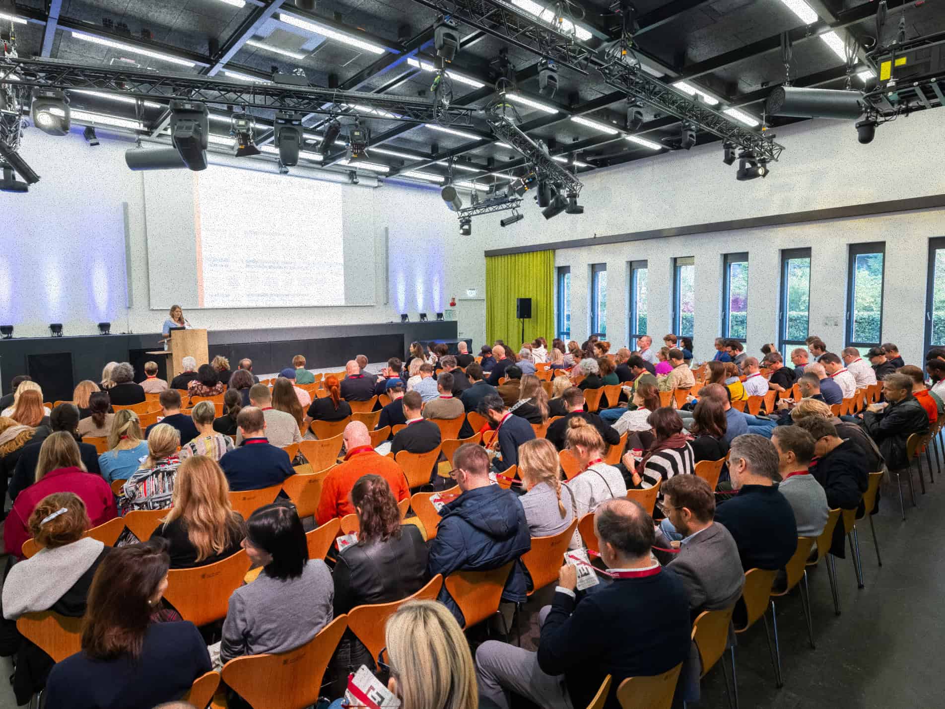 Individuals sitting in chairs listing to a speaker talk at the front of the room.